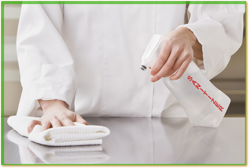 A chef wiping down a food prep counter with sanitizing liquid from a spray bottle or a bucket.